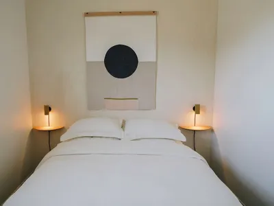 A minimalist bedroom with a white bed, wall sconces, and a geometric wall art