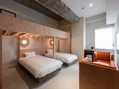 A modern hotel room featuring two beds, an orange armchair, and minimalist design elements.