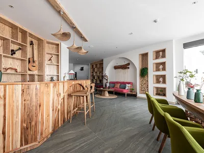 A cozy lounge area with wooden decor, including a guitar, books, and green chairs, creating a relaxing atmosphere.