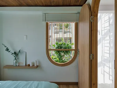 Minimalist bedroom with a bed, window, and plants, featuring wood, glass, and concrete materials.