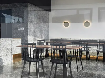Industrial-style restaurant interior with concrete and terrazzo flooring, black chairs, and minimalist design.