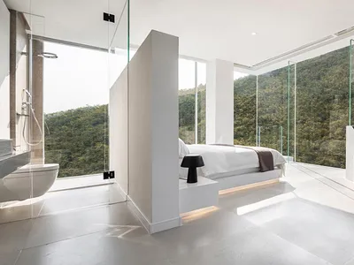 Modern bedroom featuring a glass wall overlooking a mountainous landscape.