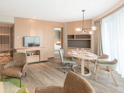 Modern hotel suite with warm-toned wood interior, featuring a dining table, chairs, and television.