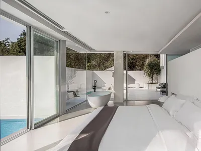Modern minimalist bedroom with glass walls and white surfaces.