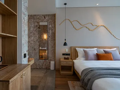 Modern minimalist bedroom featuring a bed with white bedding and orange pillows, a wooden headboard, and a side table with a