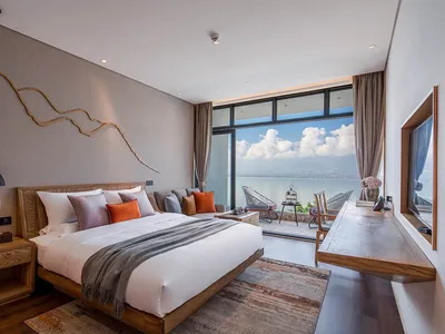 Modern minimalist bedroom with wooden platform bed, orange and gray pillows, and a sea view from the balcony.