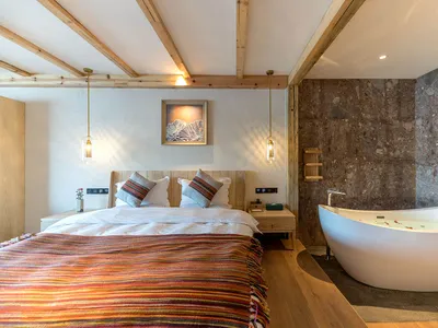 Modern minimalist bedroom with wood and marble materials, featuring a large bed with colorful textiles and a freestanding bat
