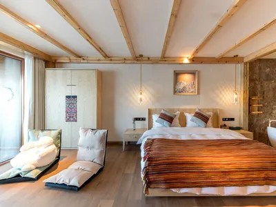 Minimalist bedroom featuring wood and stone materials, with a large bed, colorful blanket, and a bathtub.