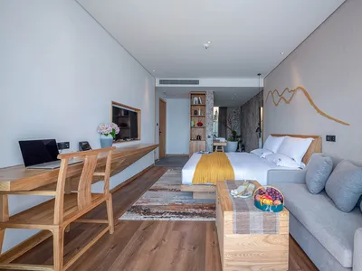 A modern hotel room with minimalist design features, including a wood desk, gray sofa, and a king-sized bed with white beddin
