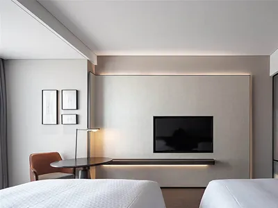 A minimalist bedroom with a modern aesthetic, featuring white beds, a TV mounted on the wall, and a floor lamp.