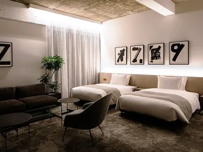 A modern hotel room with two twin beds, a brown sofa, and framed numbers on the wall.