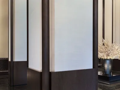 A minimalistic hotel lobby with wooden accents and a vase of flowers in the foreground.