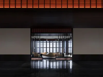 Interior view of a modern hotel lobby featuring wooden benches, glass walls, and metallic accents.
