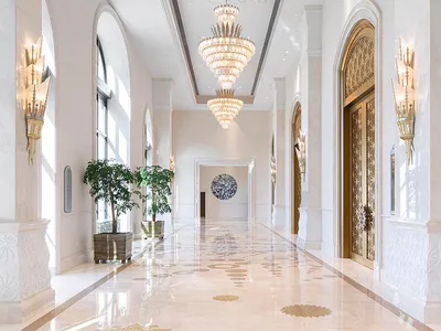 A grand, white corridor adorned with luxurious marble walls and illuminated by elegant glass chandeliers in a hotel setting.