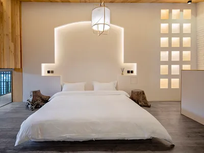 Clean, modern bedroom featuring concrete flooring, minimalist white decor, and a wooden headboard.