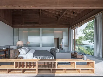 A minimalist bedroom with wooden furniture and concrete walls, featuring a large bed and a desk.