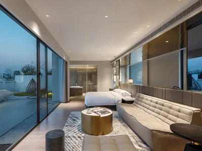 A spacious modern bedroom featuring glass walls, a large bed, and a contemporary sofa.