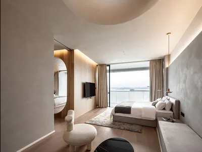 Modern minimalist bedroom featuring wooden furnishings and a circular skylight overlooking a body of water.