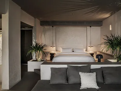 An image of a minimalist bedroom featuring a concrete bed platform and floating nightstands with leafy green indoor plants, a
