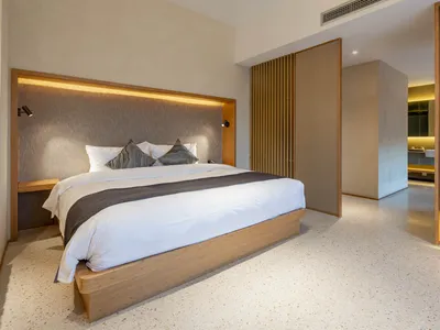 A minimalist bedroom featuring a wooden platform bed, concrete floor, and fabric headboard with embedded lighting.