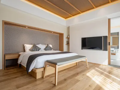 A minimalist bedroom with wooden furniture, a large bed, and a mounted television.