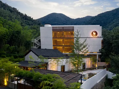 Modern, minimalist hotel resort with white stucco and glass exterior located amidst lush green mountains.