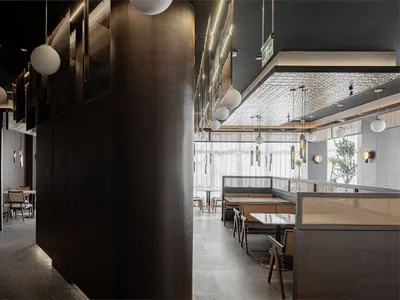 Modern restaurant interior with wooden furnishings, metallic accents, glass walls, and fabric banquettes.