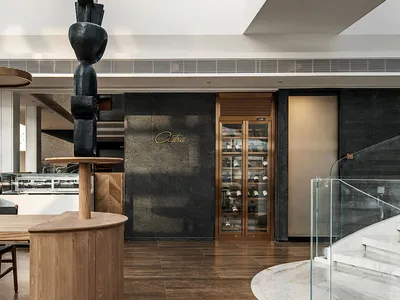 Modern restaurant entry with concrete and stone materials, featuring an abstract black sculpture.