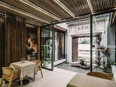 A modern restaurant interior with an indoor garden featuring a wooden table and chairs, glass walls, and concrete flooring.