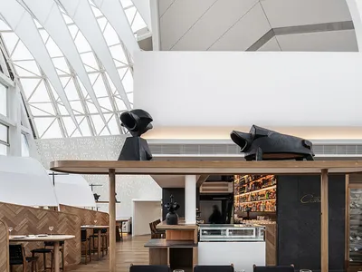 Modern restaurant interior with white walls, wood tables, concrete floor, and metal accents.