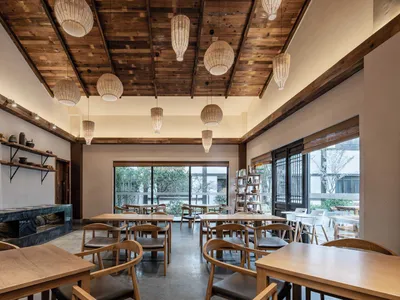 A modern restaurant interior featuring wooden beams on the ceiling and wooden tables and chairs.