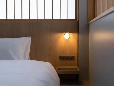 A minimalist bedroom featuring a white bed with a wooden headboard and light fixture against a wall of light grey flat panels
