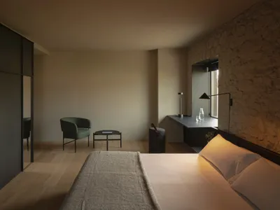 A minimalist bedroom with wooden floors, stone walls, and simple furnishings.