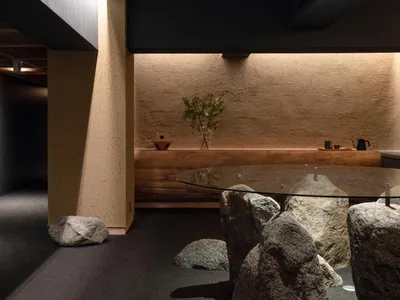 A modern restaurant interior with concrete walls adorned with rocks, a glass table, and natural elements like rocks and a vas