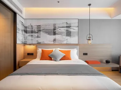 A stylish, minimalist bedroom featuring a bed with orange cushions and a gray blanket, complemented by a framed black and whi
