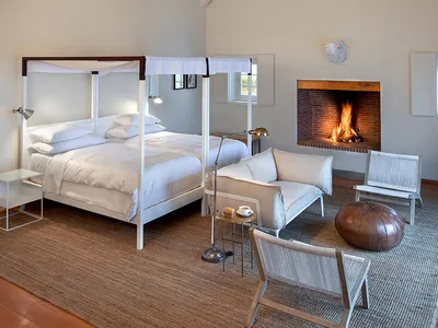 A minimalist bedroom with white furniture, a canopy bed, and a fireplace.