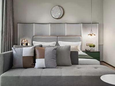 A minimalist bedroom featuring a grey fabric bed with multiple cushions, a green nightstand, and a round ceiling light.