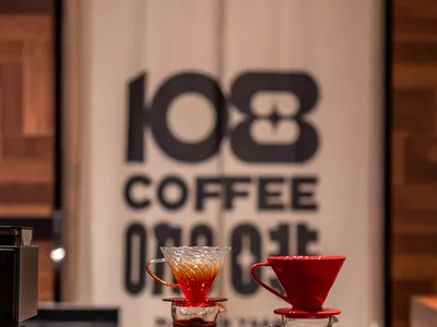 A photo of two coffee brewing tools on a counter inside a coffee shop, with a banner in the background.