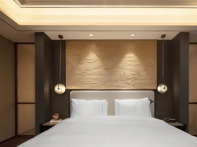 A modern minimalist bedroom interior with white bedding and patterns, featuring a decorative headboard and lighting fixtures.