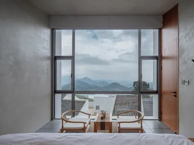 Modern bedroom with large glass window displaying scenic mountain views.