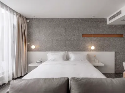 A modern minimalist bedroom featuring a grey concrete wall with floating nightstands and a white bed.