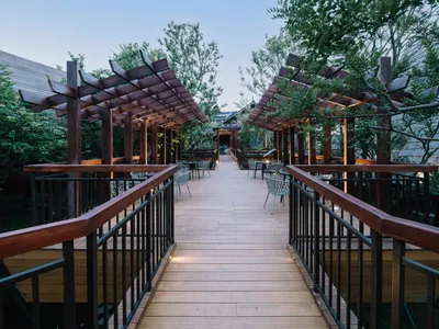 A modern outdoor restaurant with wooden pergolas and seating areas surrounded by greenery.