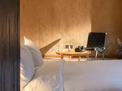 A minimalist bedroom with a white bed, wooden furniture, and a woven chair.