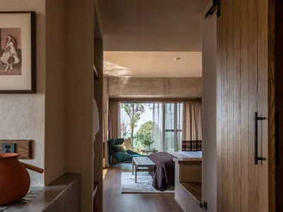 A minimalist bedroom featuring concrete walls and canvas bedding, with a large window allowing natural light to flood the spa