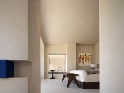 Modern bedroom with minimalist design, featuring a concrete wall, wooden furniture, and a high ceiling.