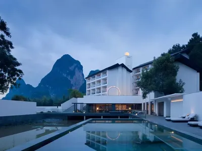 A minimalist hotel with white stone exteriors and black chevron patterns, featuring a water reflection pool.