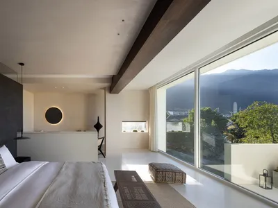 現代極簡臥室，鋪設混凝土地板、白床寢具，以及可眺望自然景觀的大窗。