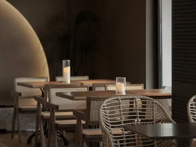 A cozy restaurant interior featuring wooden tables with woven accents, warm lighting, and potted plants