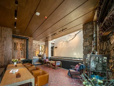 Interior of an industrial-style restaurant with wooden tables and chairs, stone fireplace, and brick walls.
