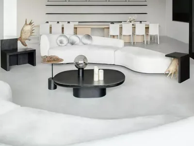 A modern minimalist living room with concrete flooring, a white sectional couch, and black coffee tables.